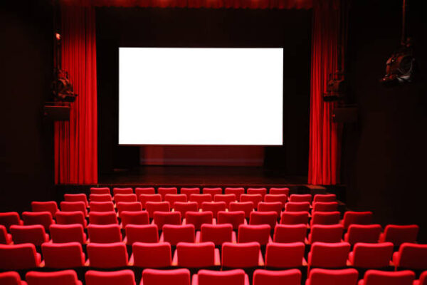 Empty cinema room with red seats and a blank white screen
